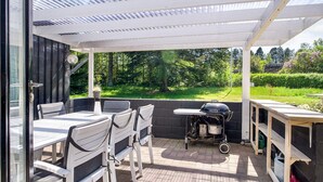 A covered patio area with a table and chairs, a grill, and a view of a garden. - 8 Person Holiday Home in Asnaes (Asnaes)