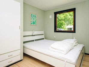 Een eenpersoonskamer met houten vloer, een wit bed, een witte kledingkast, een raam met uitzicht op bomen en een groene muur.