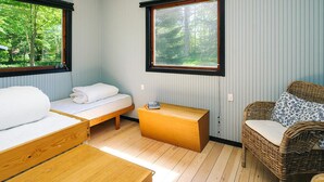 A compact room with a bed, a wooden bench, a wicker sofa, and two windows offering a forest view. - 8 Person Holiday Home in Asnaes (Asnaes)