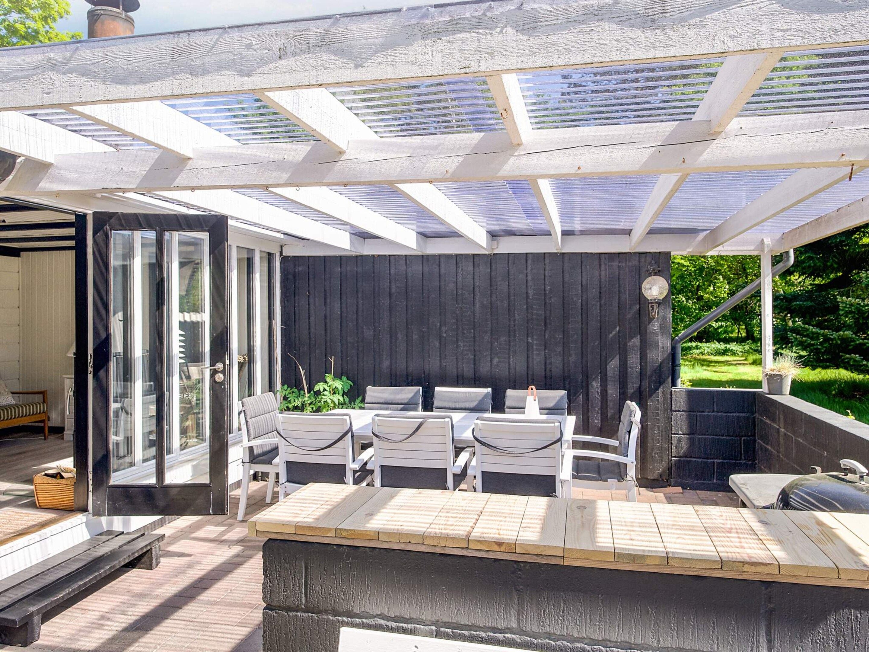 An outdoor patio with a wooden deck, white chairs, and a glass door leading to an interior space.