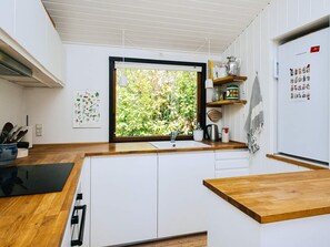 Eine moderne Küche mit weißen Schränken, einer Holzarbeitsplatte, einem Fenster mit Blick ins Grüne und einem Kühlschrank mit Magneten.