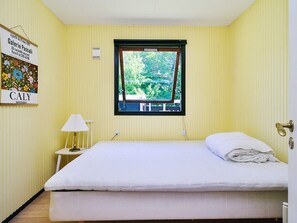 Ein Zimmer mit einem Bett, einem Fenster mit Blick auf Grünflächen, einem kleinen Tisch mit einer Lampe und einem Wandzeichen.