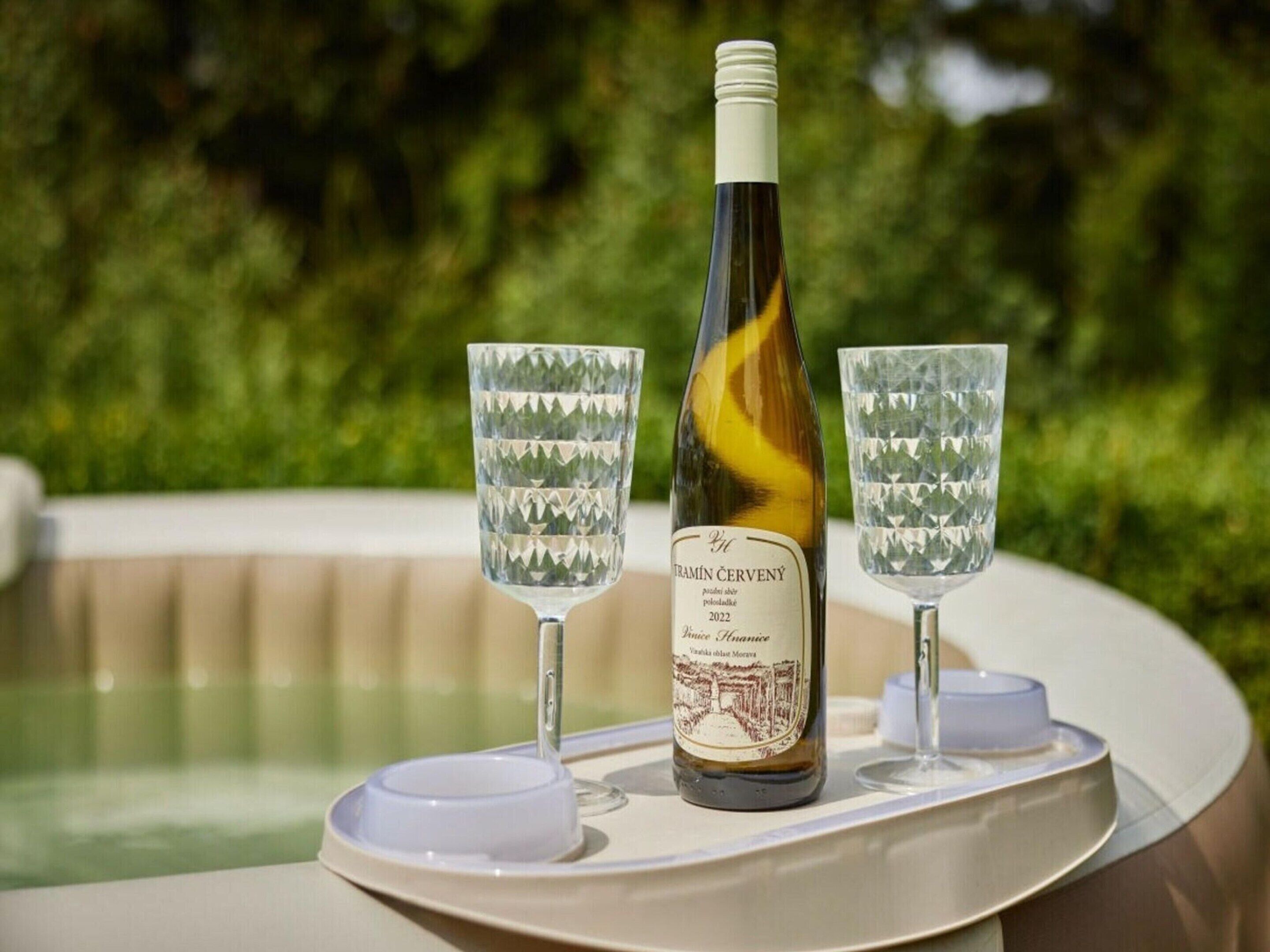 A bottle of wine and two glasses on a tray by a pool.