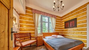 Dormitorio de una cabaña de madera con cama, banco y ventana con cortinas.