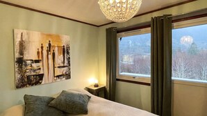 A hotel room with a large bed, a chandelier, a painting on the wall, and a window with curtains. - 12 Person Holiday Home in Davik (Bremanger)