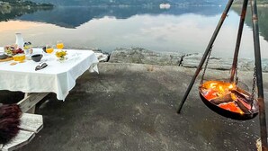 A table set with breakfast items and a hanging fire pit by a lakeside. - 12 Person Holiday Home in Davik (Bremanger)