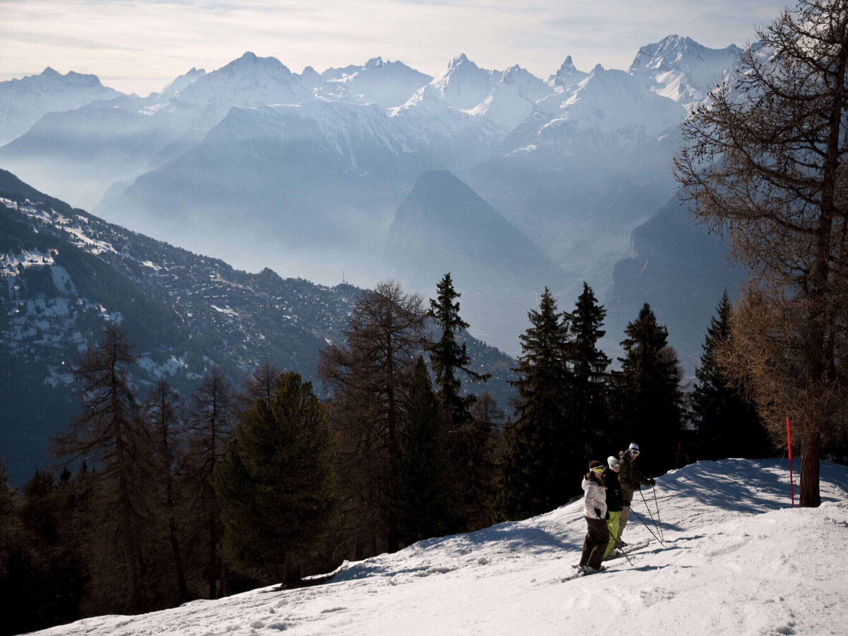 A snowy mountain landscape with a ski slope, trees, and distant peaks.