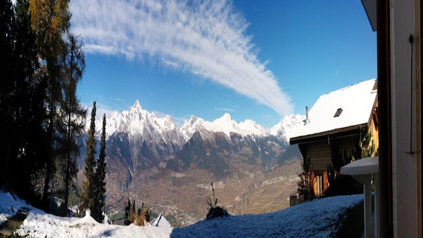 Paesaggio innevato con una catena montuosa sullo sfondo e un edificio con tetto spiovente.