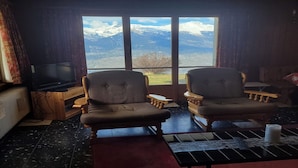 Una stanza con due poltrone, una televisione e vista sulle montagne innevate attraverso ampie finestre.