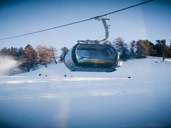 A ski lift chair suspended by a cable, with a snowy slope and trees in the background. - Sunny Apartment With Outdoor Dinning (Veysonnaz)