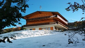 Un chalet in legno a più piani con balconi, situato su un pendio innevato.