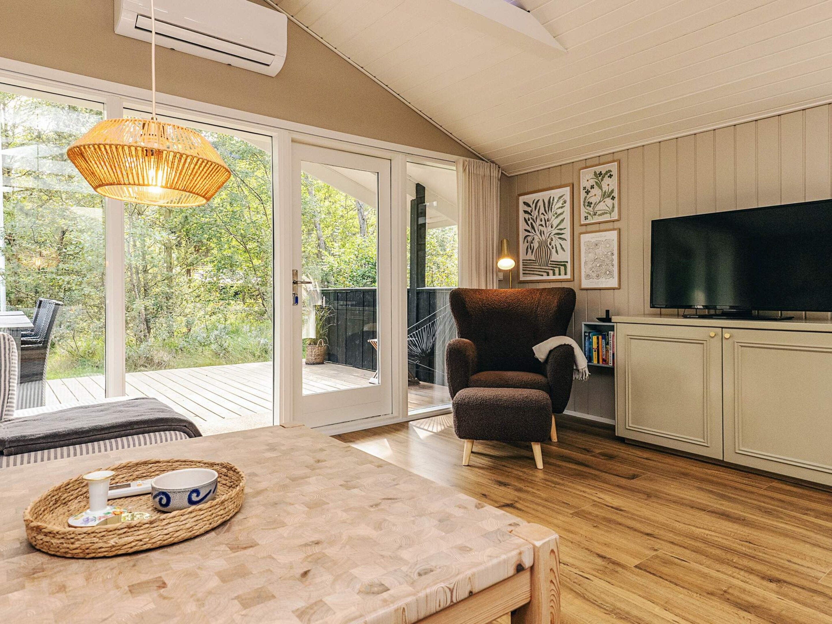 A room with a wooden floor, a sofa, a television, and a large window.