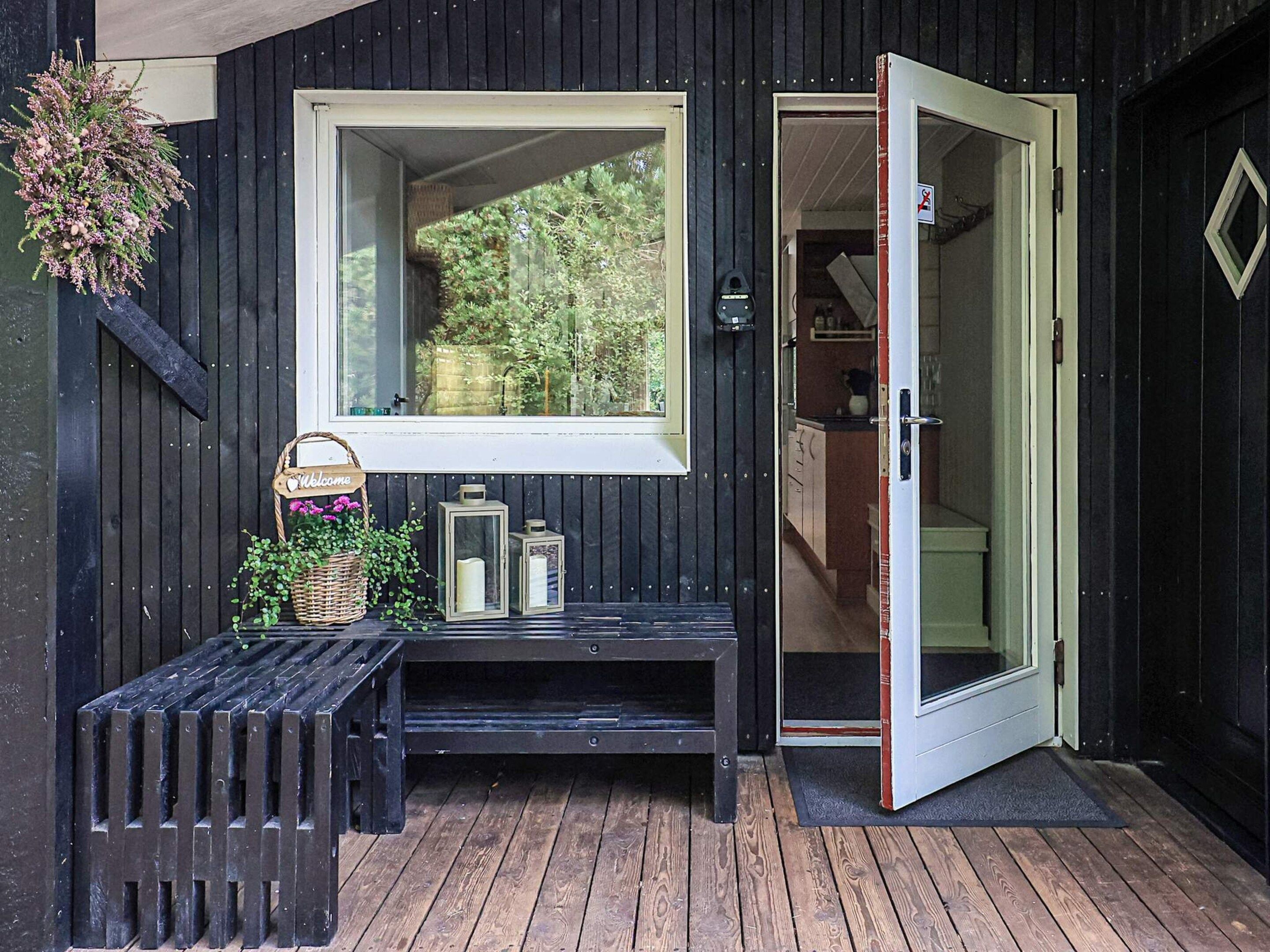 A wooden exterior with a door, a bench, a welcome sign, and a window.