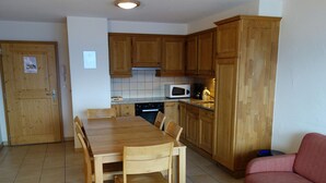Eine kompakte Küche mit Holzschränken, einem Esstisch mit Stühlen, einer Mikrowelle und einem roten Sofa.