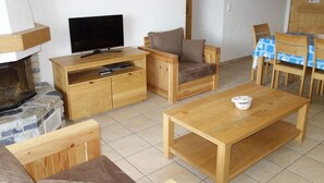 Ein gemütliches Wohnzimmer mit Fernseher, Holzmöbeln, Kamin und Essbereich mit Tisch und Stühlen.