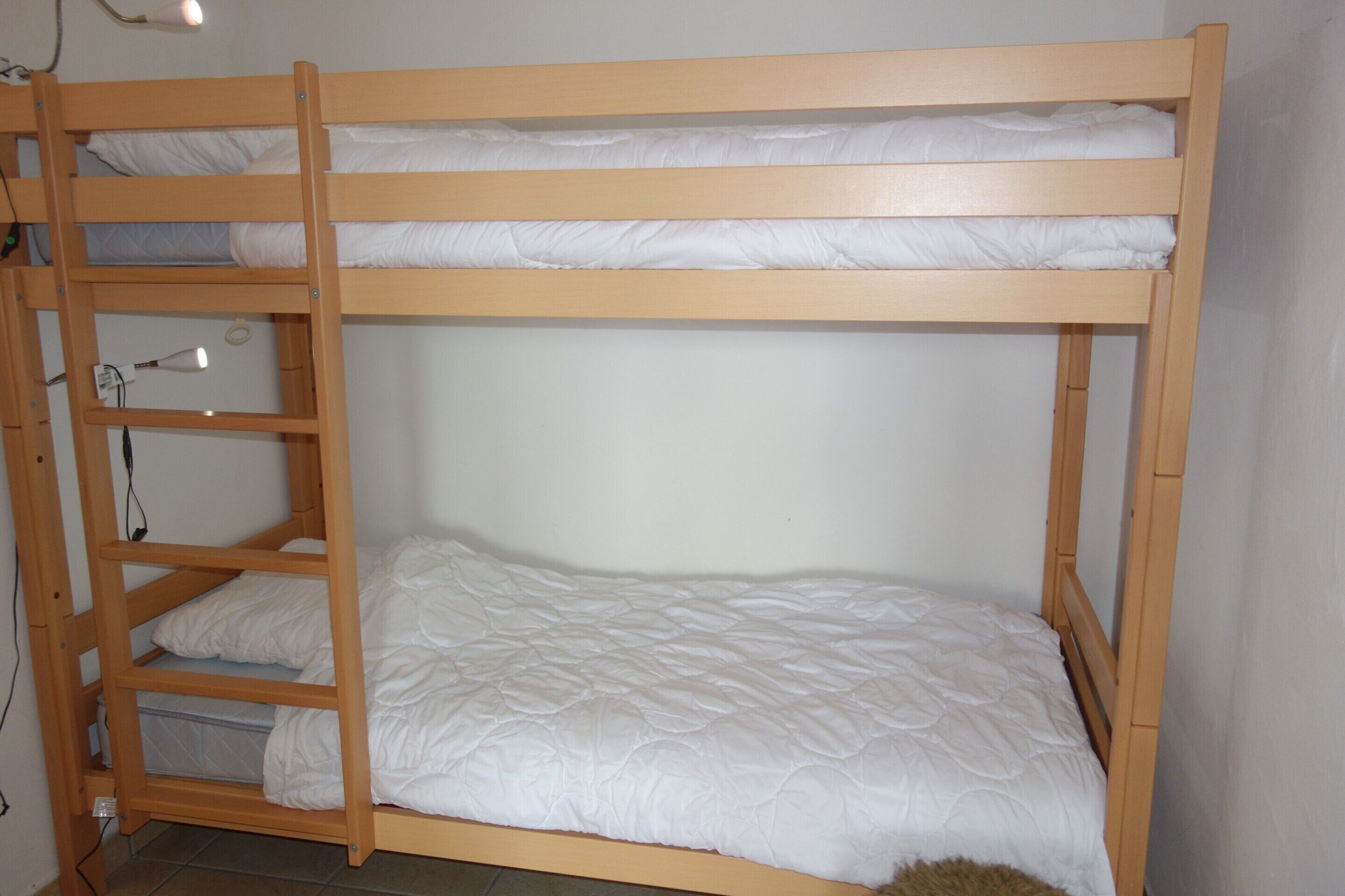 A bunk bed with a wooden frame and white bedding.