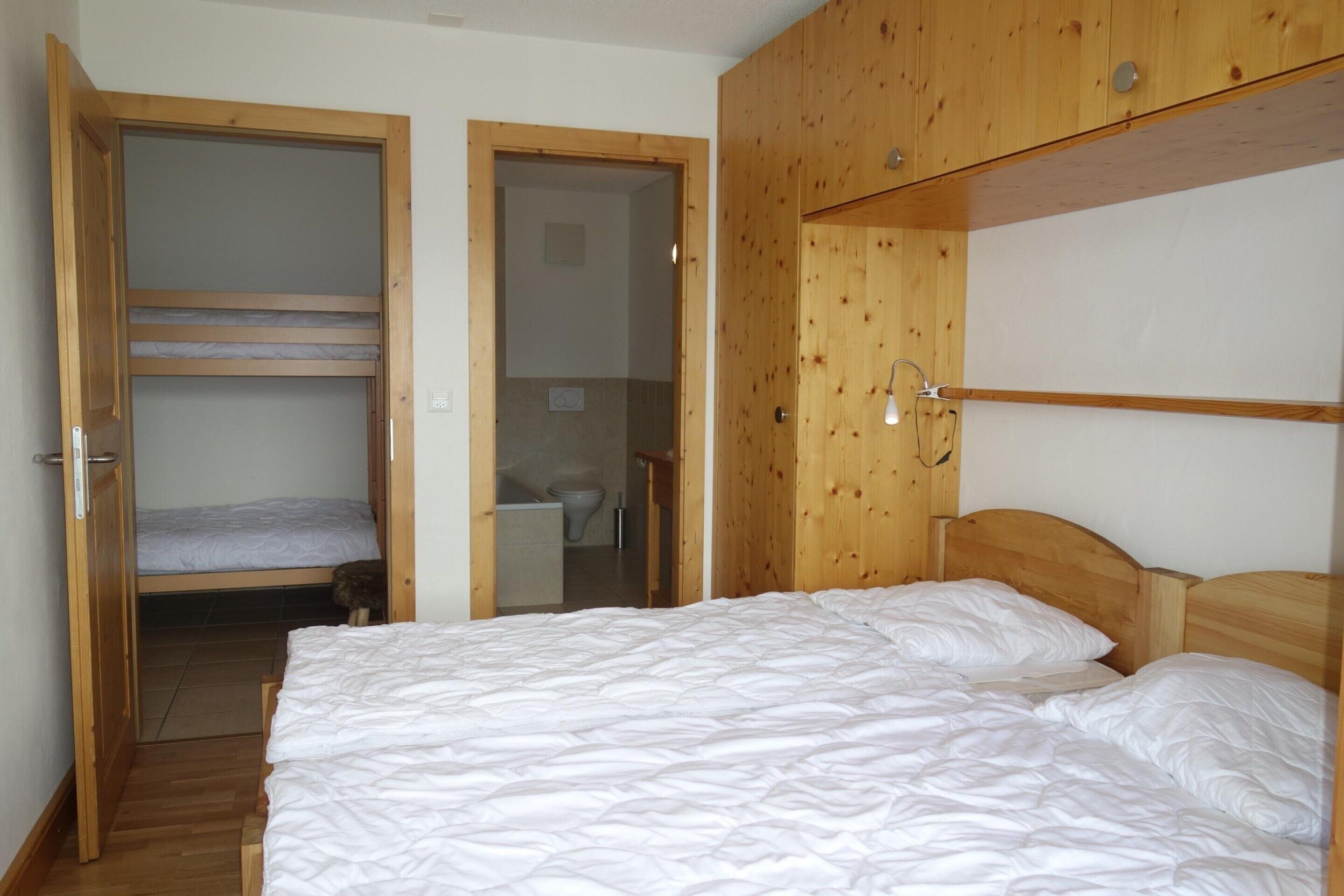 A room with a bunk bed, a wooden wardrobe, and a small bathroom.