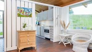 A kitchen with white cabinets, a wooden chest of drawers, and a dining area with a wicker chair and a table. - 5 Person Holiday Home in Aabenraa (Aabenraa)