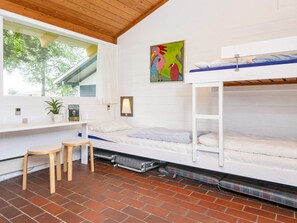 A bunk bed room with a window, a desk, a chair, and a painting on the wall.