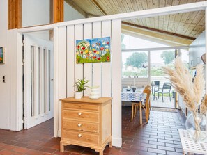 A room with a wooden dresser, a painting of flowers, and a view of an outdoor patio with chairs and a table.