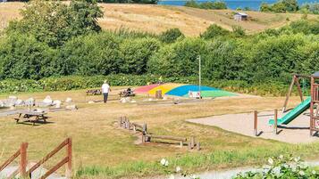 Un parque con mesas de picnic, un parque infantil y una vista panorámica del agua.