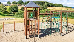 A playground with a wooden climbing structure and a netted play area. - 5 Person Holiday Home in Aabenraa (Aabenraa)