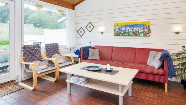 A room with a red sofa, two wooden chairs, a white table, and a painting on the wall. - 5 Person Holiday Home in Aabenraa (Aabenraa)