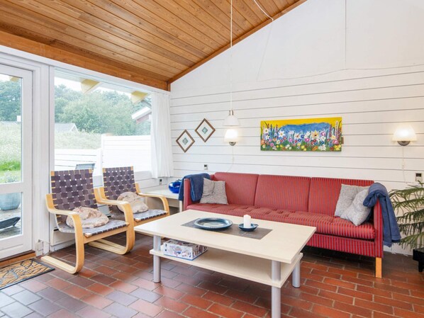Una habitación con un sofá rojo, dos sillas de madera, una mesa blanca y un cuadro en la pared.