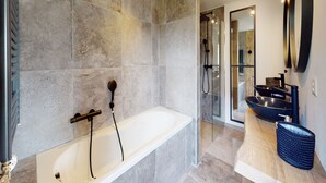 Ein modernes Badezimmer mit einer großen Badewanne, einer gläsernen Dusche und einem Waschtisch mit Waschbecken und Spiegel.