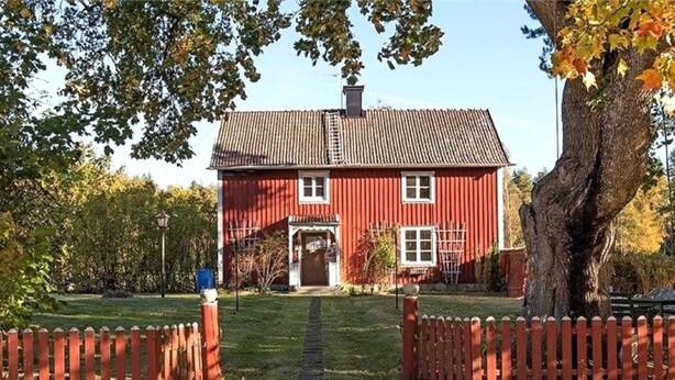 A red wooden house with a tiled roof, a front door, and a small porch.
