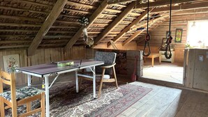 A rustic attic room with a ping pong table, a patterned rug, wooden furniture, and a sloped ceiling with exposed beams.