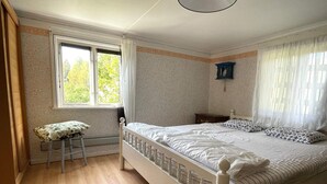 A bedroom with a wooden floor, a bed with white bedding, a window with curtains, and a small stool.