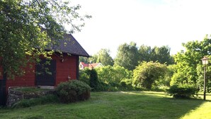 A red wooden building with a sloped roof, surrounded by a well-maintained lawn and various shrubs.