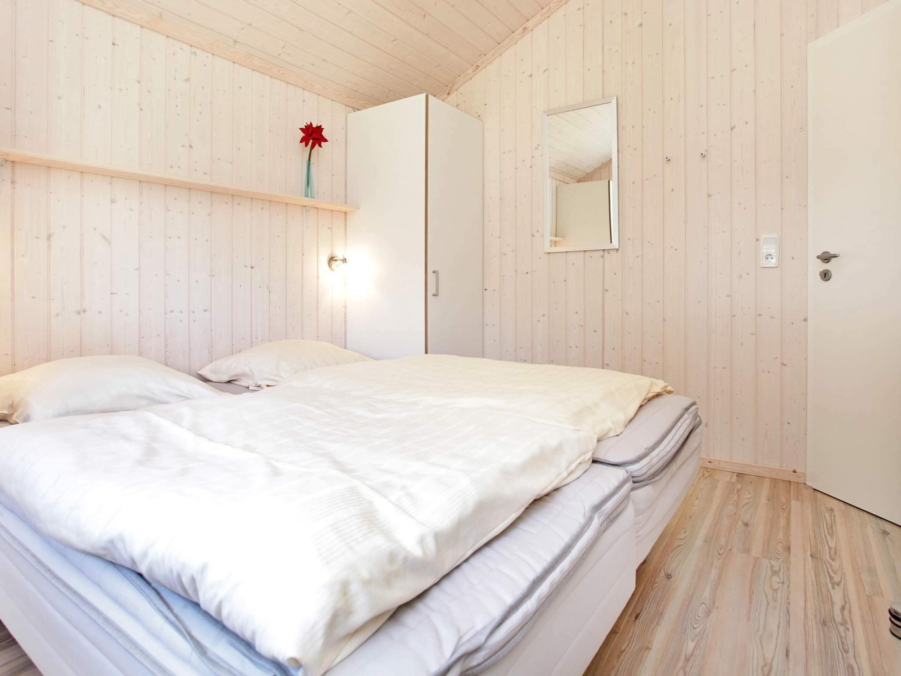 A bedroom with a bed, a wardrobe, a mirror, and a wall-mounted light fixture.