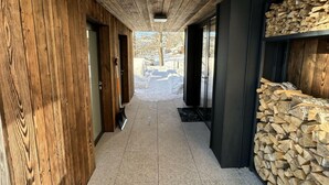 A corridor with wooden walls and a tiled floor, leading to a door and a stack of firewood. - Cerny Dul Kcmv115 Comfortable Holiday Residence (Cerny Dul)