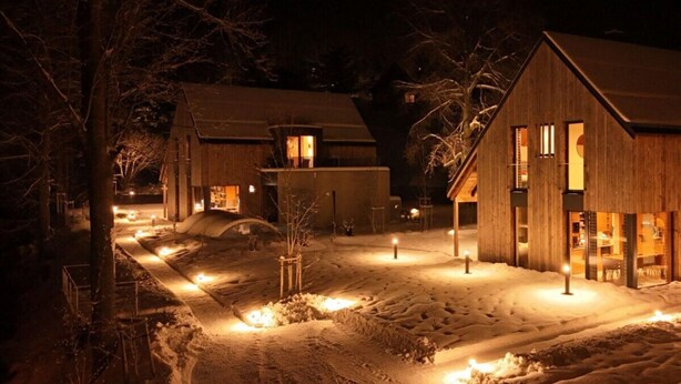 A snow-covered courtyard with wooden buildings, illuminated windows, and a clear path. - Cerny Dul Kcmv115 Comfortable Holiday Residence (Cerny Dul)