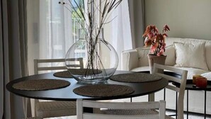 Ein Essbereich mit einem runden Tisch, weißen Stühlen und einer Vase mit Zweigen.