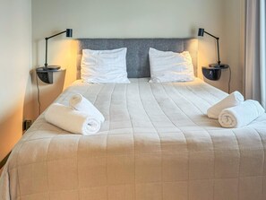 Un lit bien fait, avec deux oreillers, deux tables de chevet avec des lampes et deux serviettes enroulées posées sur le lit.
