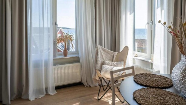 Ein Zimmer mit Meerblick, ein Sessel, ein Tisch mit gewebten Untersetzern und ein Blumentopf.