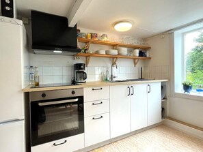 A kitchen with white cabinets, a built-in oven, a coffee maker, and a window with a view of greenery.