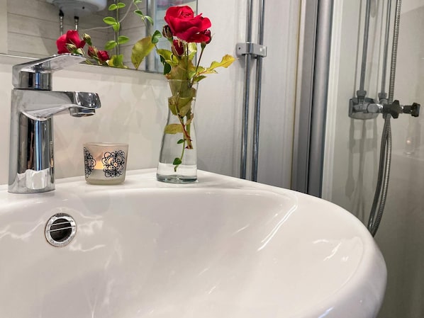 A bathroom with a white sink, a chrome faucet, a glass vase with a red rose, and a candle with a black floral design.