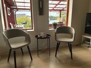 A room with two chairs, a small table, a TV, and a view of a body of water through a window. - 4 Person Holiday Home in Figeholm (Figeholm)