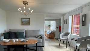 Un saló modern amb un sofà gris, una taula de centre de fusta i un armari gris. Hi ha un quadre a la paret i una finestra amb cortines.