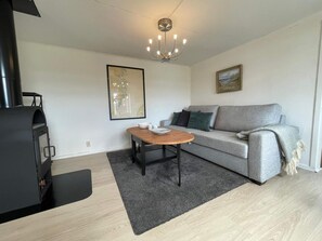 A modern living room with a sofa, a wooden coffee table, a black fireplace, and a chandelier. - 4 Person Holiday Home in Figeholm (Figeholm)