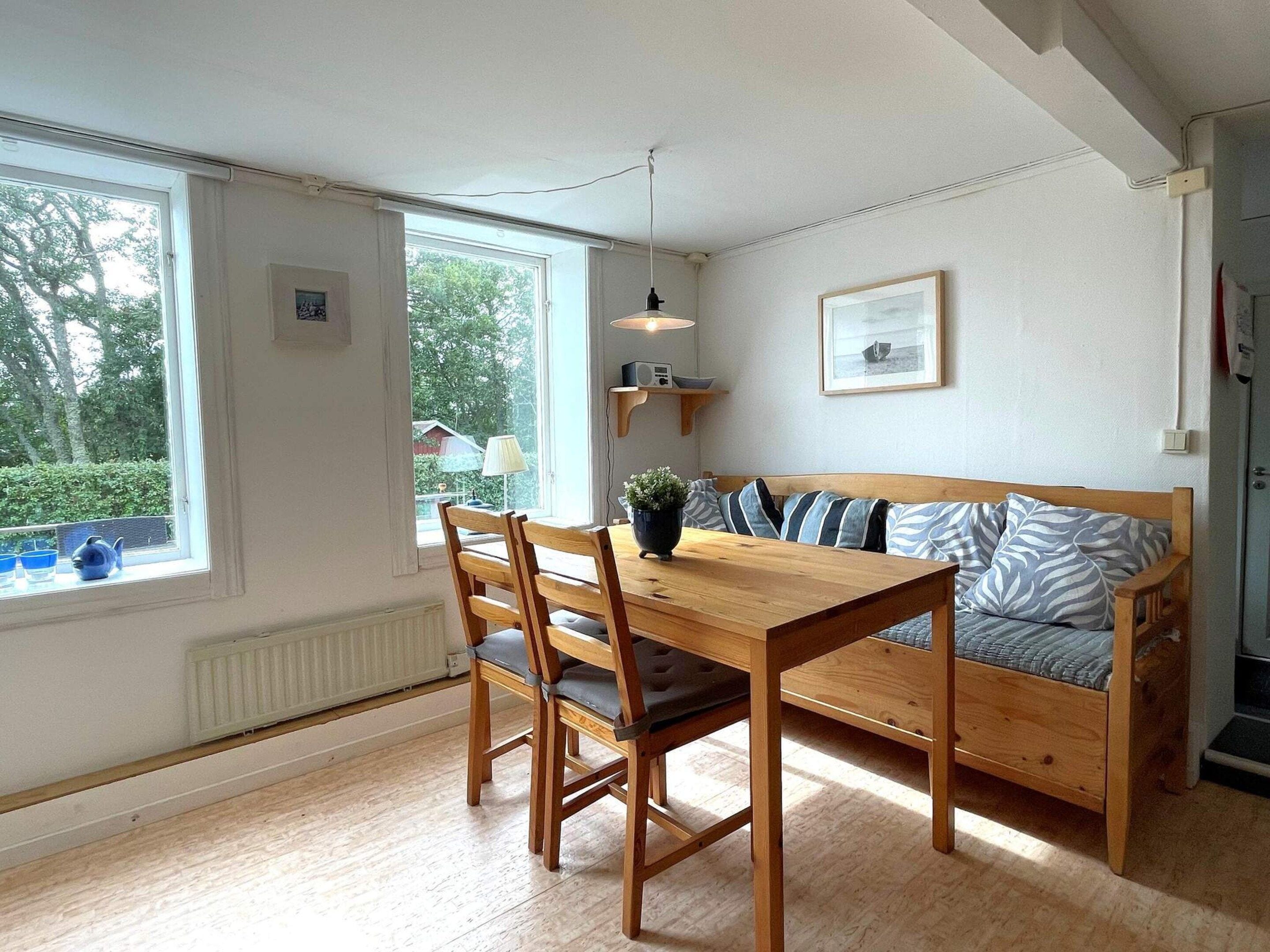 A dining area with a wooden table and chairs, a bench with cushions, a hanging light fixture, and a view of the outdoors through a window.