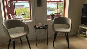 Una habitación con dos sillas, una mesita, televisor y ventana que da a vistas de vegetación y un muelle.