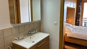 A modern bathroom with a white sink, wooden vanity, and a mirror. - Pleasant Apartment With Balcony (Veysonnaz)