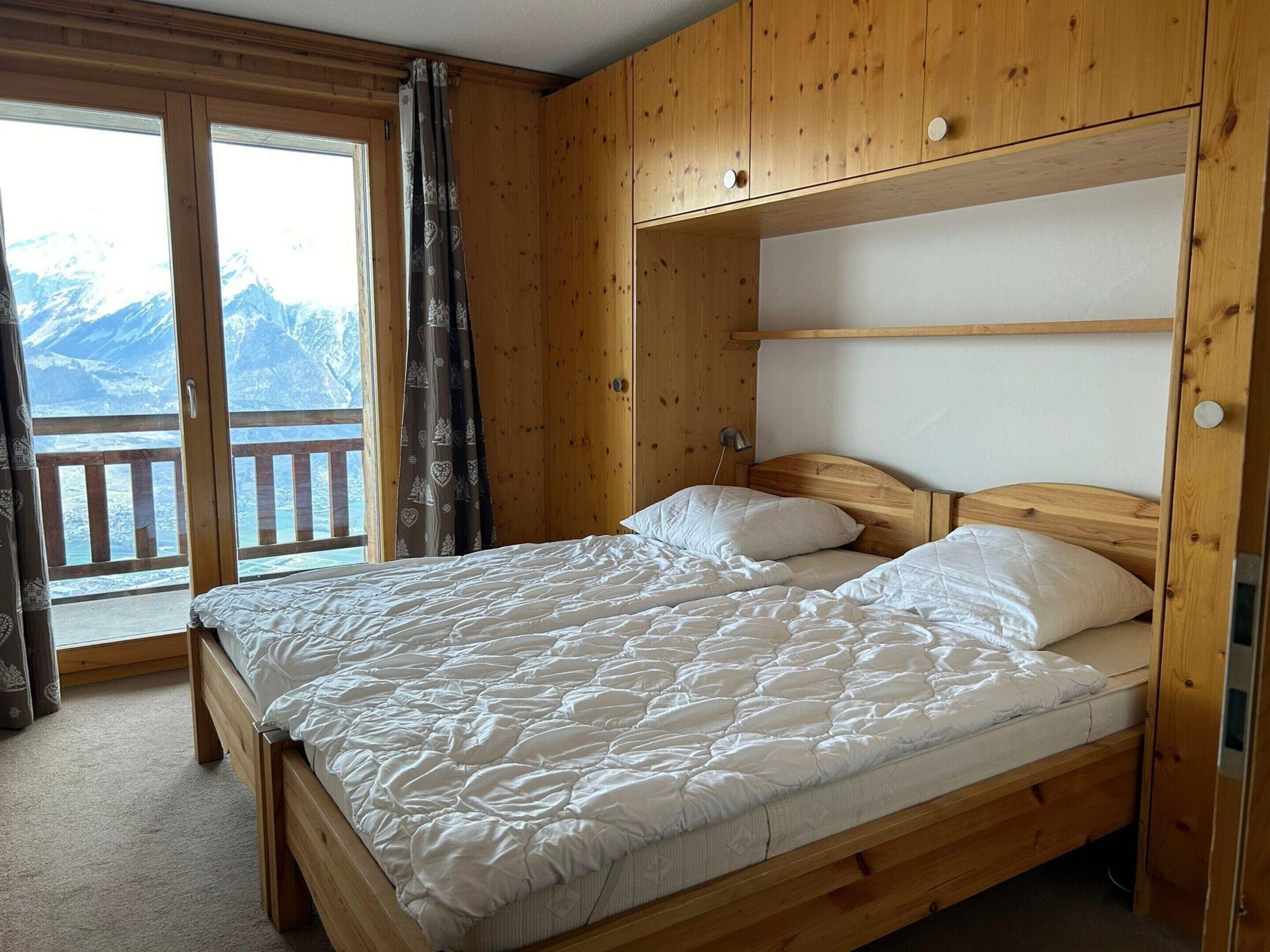 A wooden bedroom with a bed, a nightstand, and a view of mountains through a large window.