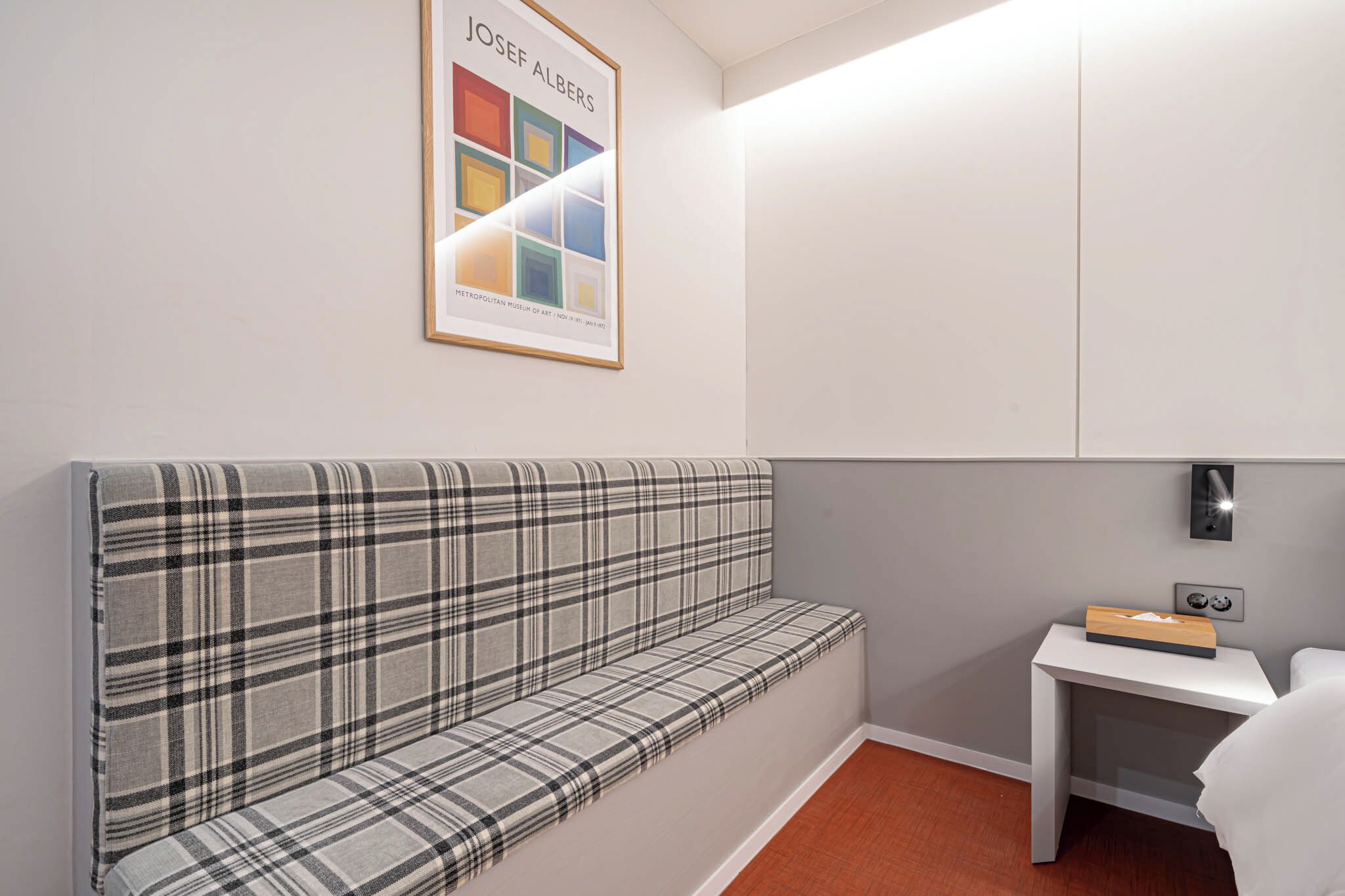 A modern room with a plaid sofa, a small bedside table with a tissue box, and a framed artwork on the wall.