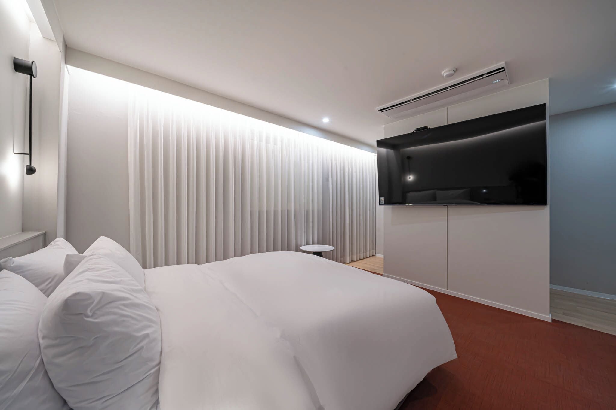 A modern hotel room with a large bed, a small round table, a TV mounted on the wall, and an air conditioning unit.